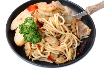 Stir fried spicy spaghetti with shrimp, clam, sausage, ham and dried chili on black plate. Asian meal concept.