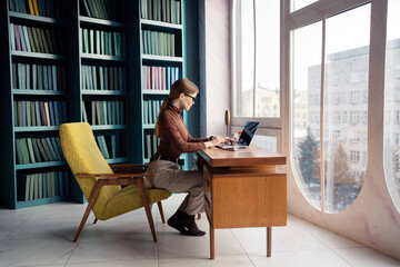 The manager is a woman with glasses working in an office coworking space workplace, uses a laptop writes a message