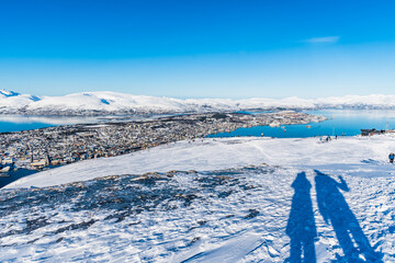 Shadow of a couple standing on the top of Storsteinen mountain overlooking the city of Tromso in northern Norway, copy space