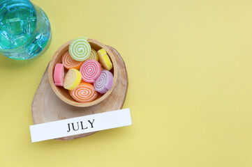 Hello July, July text on white wood block and jelly sweet on yellow background. summer season and hello july concept.