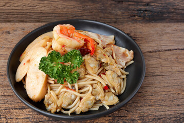 Homemade Stir fried spicy spaghetti with shrimp, clam, sausage, ham and dried chili on old wooden table. Asian meal concept.