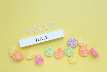 Hello July, July text on white wood block and jelly sweet on yellow background. summer season and hello july concept.