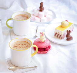 A cup of hot coffee with text Happy Easter written on cream mousse, with rabbit chocolate and cake decoration in festive atmosphere, latte art 