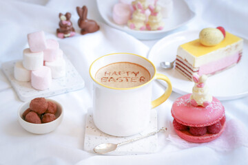 Fototapeta na wymiar A cup of coffee with written Happy Easter text on cream mousse and Easter rabbit chocolate and cake decoration atmosphere, latte art 