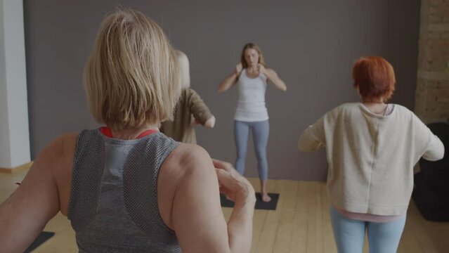 Rear of mature women practicing body tapping with female Caucasian yoga instructor in class
