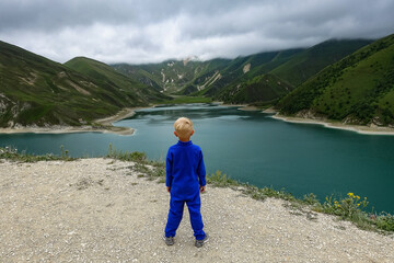 Fototapeta na wymiar A boy on the background of Lake Kezenoy-am in the Caucasus mountains in Chechnya, Russia June 2021.