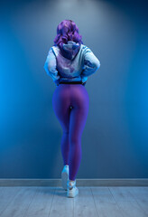 a girl in stylish purple sportswear and with purple hair poses sexually with her back