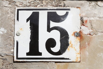 Altes verwittertes weisses Hausnummernschild Nummer Fünfzehn aus Metall an einer Hauswand