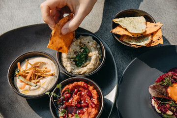 Various aperitif humus dishes with grilled pita. Closeup of human hand dipping pita in humus.