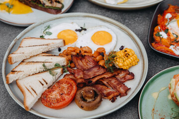Closeup of an english breakfast. Fried eggs with bacon, beans, corn and vegetables.