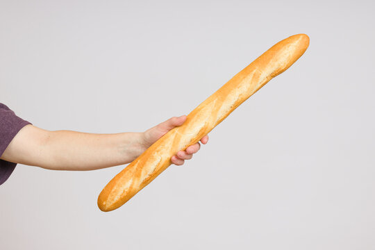 long bread baguette in a female hand on a white background close-up