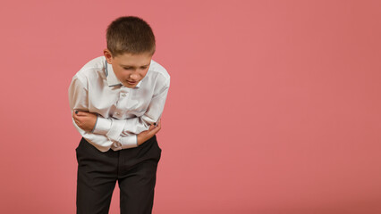 an elementary school student in a white shirt holds his hands on his sore stomach on a colored background
