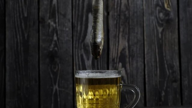 salted, dried vobla fish revolves over amber beer on dark wooden background in a minimalism style