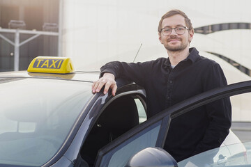 Portrait of smiling caucasian taxi driver near car, looking at camera.