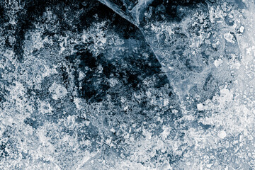 Ice texture background. The textured cold frosty surface of the ice with cracks on the dark blue...