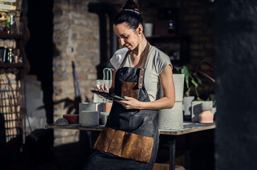 Portrait of craftswoman in apron in her workshop holding tablet.