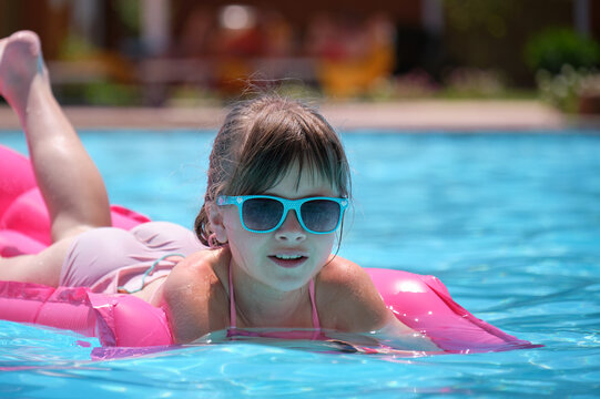 Young child girl relaxing on summer sun swimming on inflatable air mattress in swimming pool during tropical vacations. Summertime activities concept - Powered by Adobe