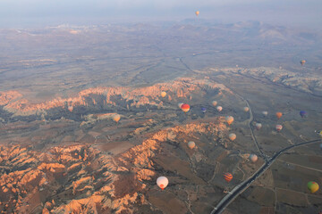 A lot of hot air balloons are flying over the valley with road in Cappadocia. Aerial photography
