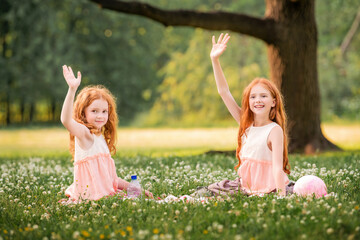 Portrait of two red-haired happy girls lying among white clover flowers