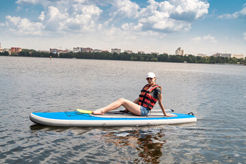  young woman wear life vest paddle boarding on a lovely lake at summer hot day