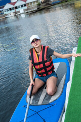 pretty slim woman floats on sup board and long paddle on city lake