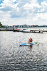 Fototapeta na wymiar pretty slim woman floats on sup board and long paddle on city lake