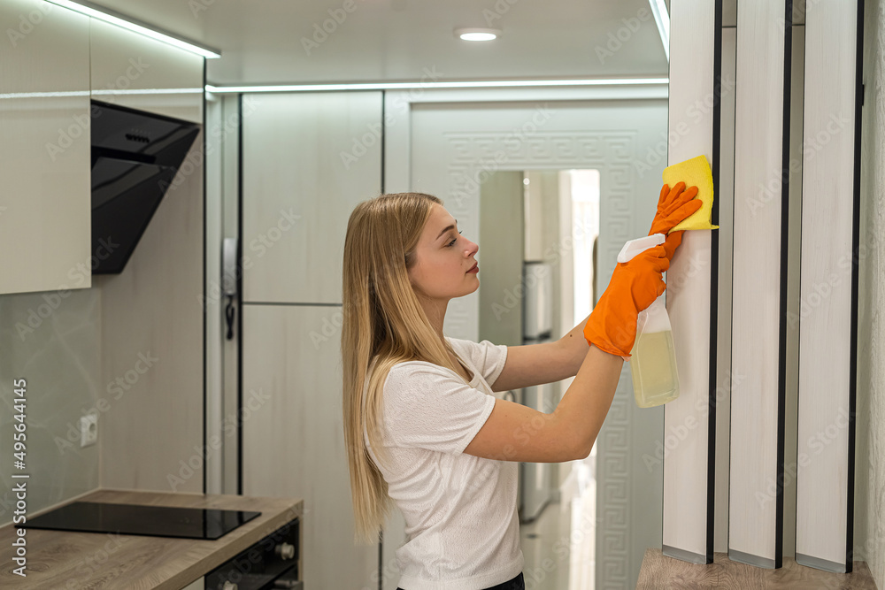 Wall mural Young housewife cleaning the kitchen with rubber and special spray