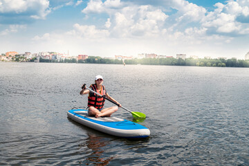 Fototapeta na wymiar Charming smiling woman rides a sup paddle board around city lake