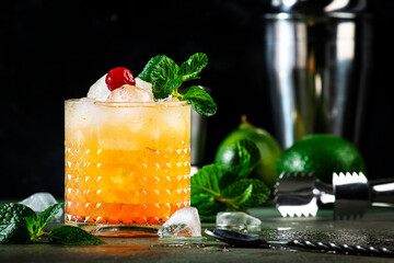 Mai Tai trendy alcoholic cocktail with rum, liqueur, syrup, lime juice, mint and crushed ice. Dark background, bar tools, copy space