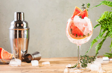 Gin tonic trendy alcoholic cocktail drink with dry gin, bitter tonic, lemon juice, grapefruit, thyme and ice with bar tools. Wooden table background with copy space