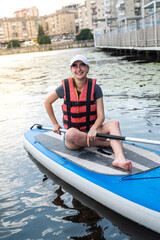 pretty slim woman floats on sup board and long paddle on city lake
