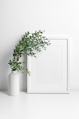Frame mockup over white wall with fresh eucalyptus plant in vase, copy space for artwork, photo or print presentation