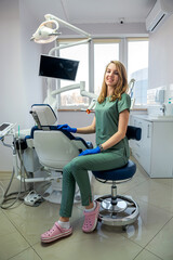 Young woman dentist in uniform and protection gloves posign alone at clinic