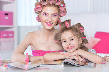 Obraz na płótnie Canvas Mother and little daughter with hair curlers reading magazine