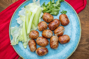 Thai isaan , isan sausage, Sai krok Isan, with cucumber, coriander and lettice on a turquoise plate.