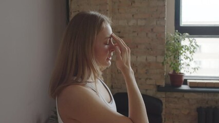Chest-up of young Biracial female yoga instructor standing with eyes closed in studio at daytime, showing pranayama breathing technique and talking