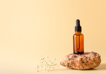 Cosmetic bottle with dropper mockup on stone on beige background. Face serum or essential oil in brown glass vial. Eco skincare concept.