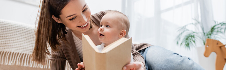 Positive parent holding book near baby at home, banner.