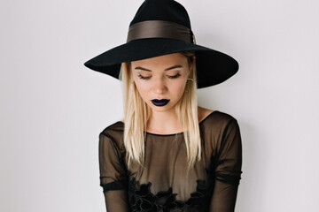 Fototapeta na wymiar Studio close up portrait of pretty woman with dark lips is wearing hat and blouse is looking down over isolated background