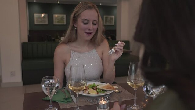 Pretty blonde woman at dining table eating lunch with friend in fancy restaurant