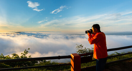 Panorama photographer standing on top of Mountain at sunset with Mist.Asian male backpack in nature during sunset Relax time on holiday concept travel at Pha mor i dang,Sisaket province,Thailand,ASIA. - obrazy, fototapety, plakaty
