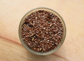 Flax seeds affected by pests. Glass plate with flax seeds on a wooden surface. Dietary fibers of...