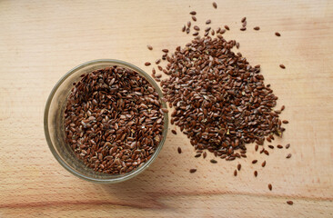 Flax seeds affected by pests. Glass plate with flax seeds on a wooden surface. Loose flax seeds on...