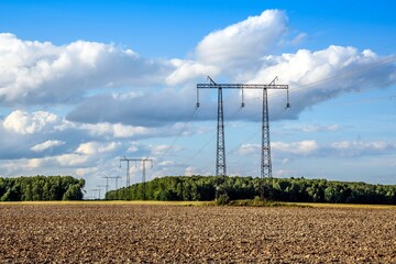 An electric power transmission line on steel supports and a plowed field in the early summer evening. Power lines
