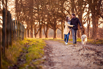 Fototapeta premium Couple With Woman With Prosthetic Hand Walking Pet Dog Through Winter Or Autumn Countryside