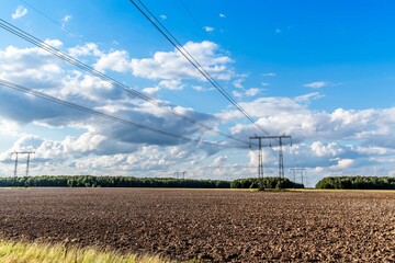 Electric power transmission lines on steel supports and a large plowed field in the early summer evening under a beautiful sky. Power lines.