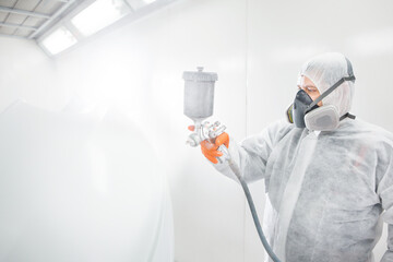 Male worker painting a car in a white paint booth.