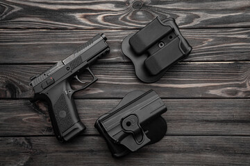 Pistol and plastic holster on a wooden back. A short-barreled weapon and a flashlight near the...