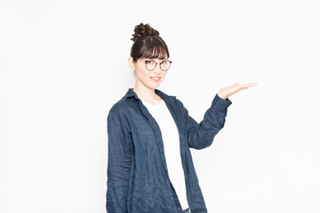白い背景の前に立って案内のジェスチャーをする眼鏡をかけている女性