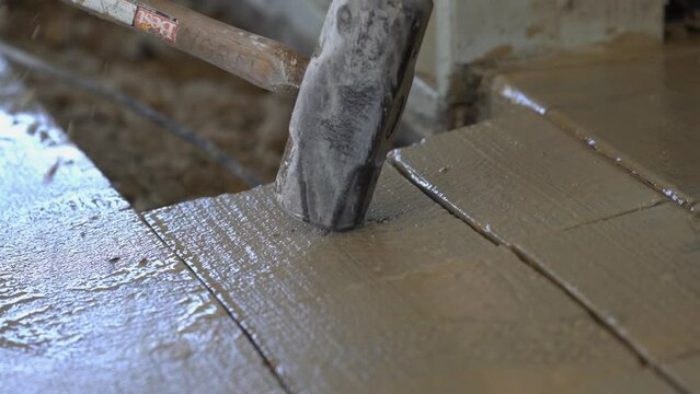 A construction worker breaking up concrete with a sledge hammer